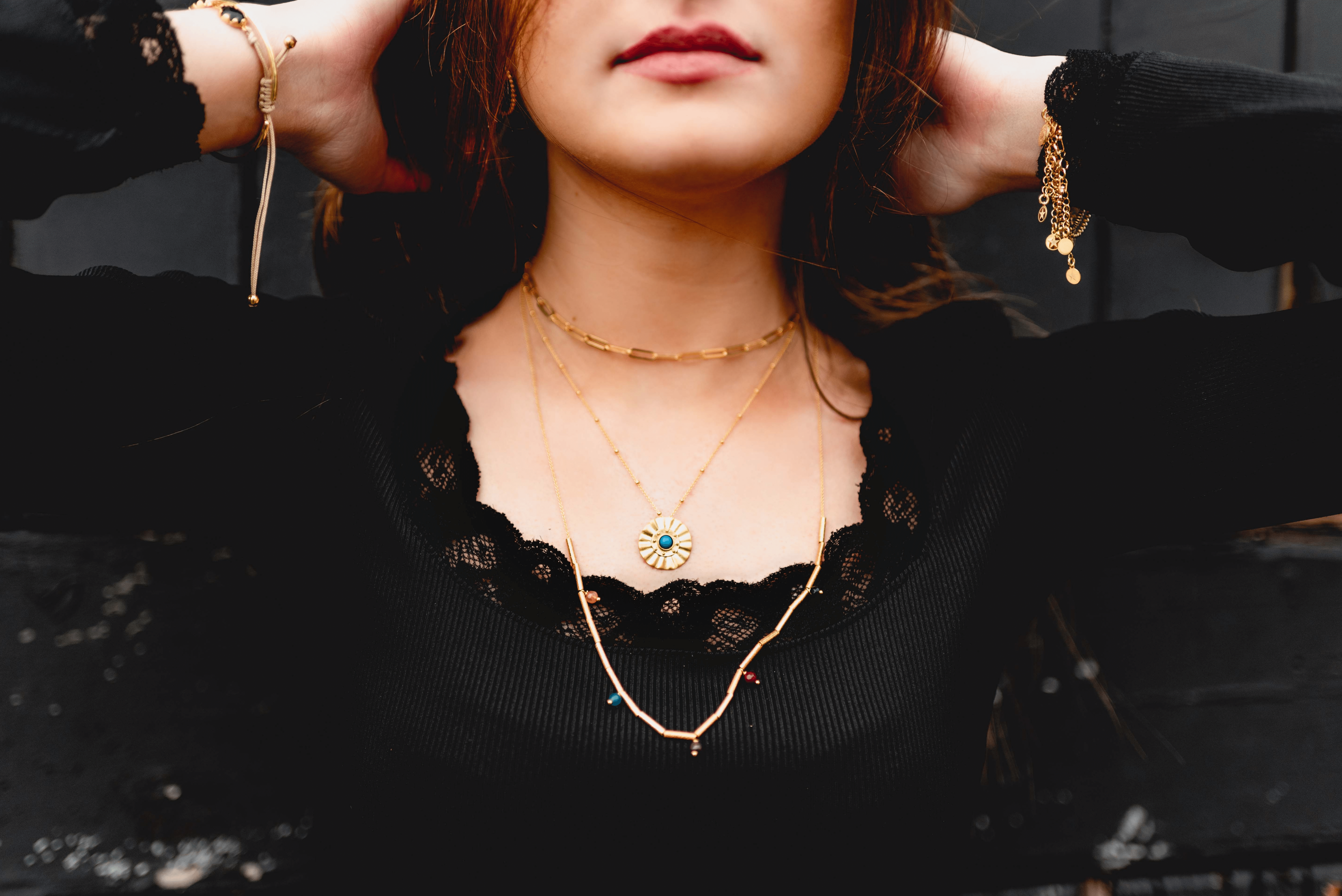 Influenstar Jewellery model with dark hair and black top wears three gold necklaces